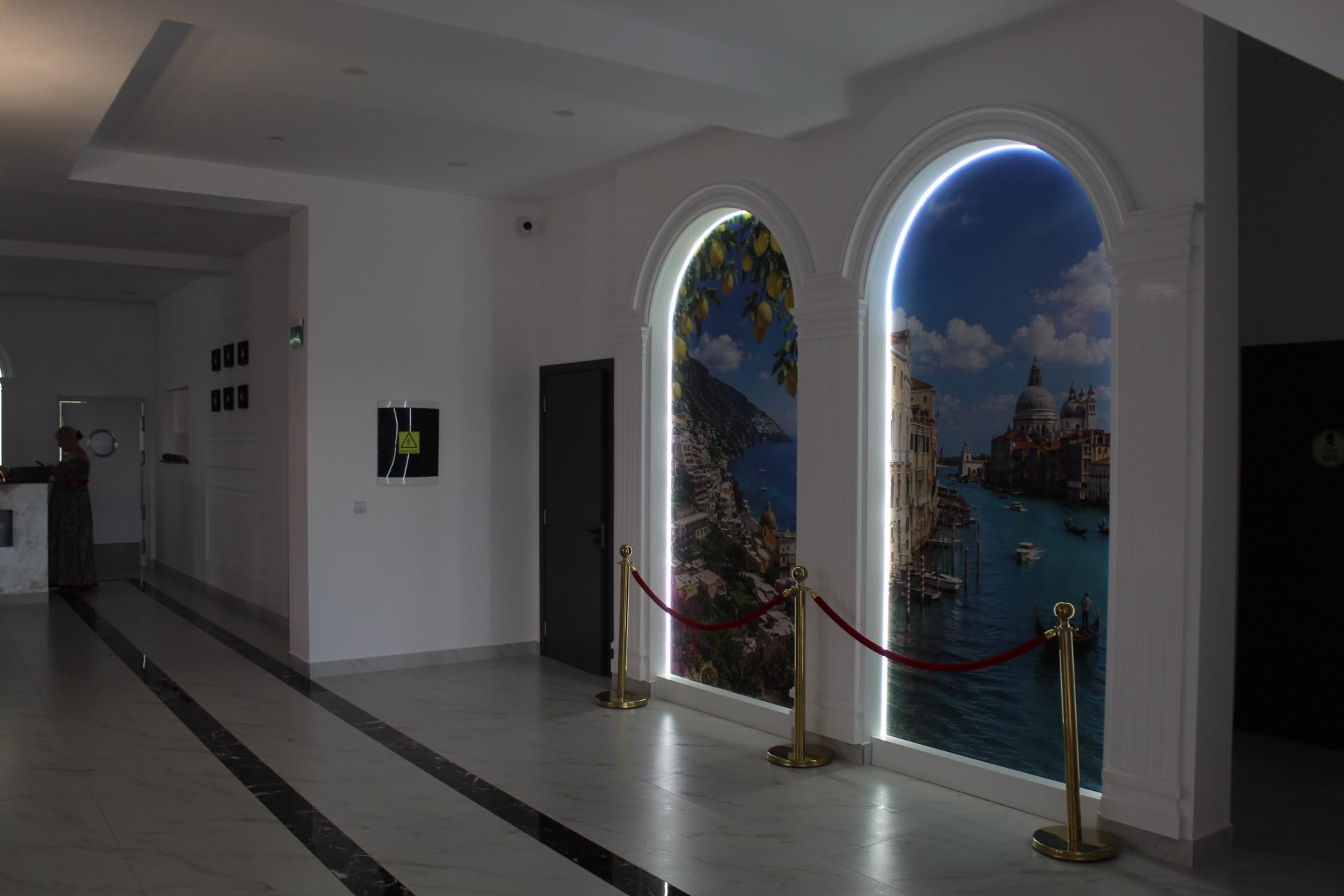 Un coridor discret la Giovanni's, cu două arcade iluminate din spate care înfățișează Amalfi și Veneția, podea de marmură și stâlpi de alamă cu șnur